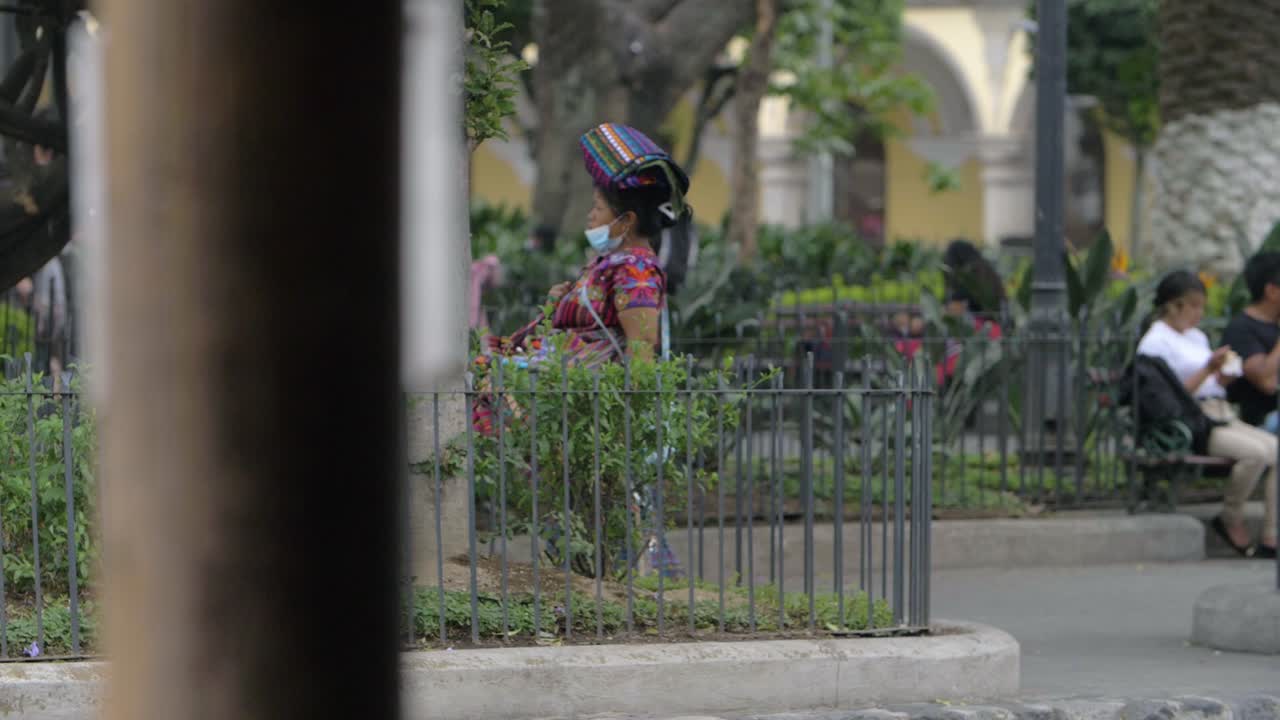 Antigua Guatemala woman wears traditional colorful handmade dress, walking on main town square with various souvenirs for sale, wearing face mask due to recent Covid-19 pandemic - Slow motion