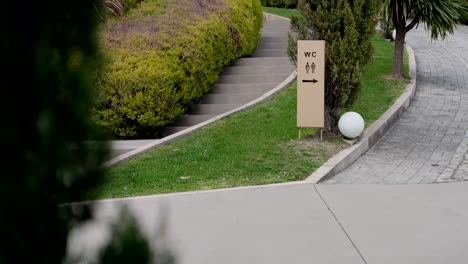 wc sign with arrow stands beside pathway and greenery in outdoor garden area