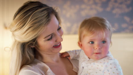 loving mother cuddling baby daughter at home in nursery