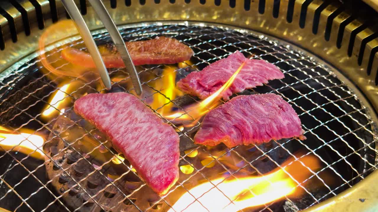 Primo piano di carne di manzo cruda marmorizzata che cuoce su una griglia a carbone con fiamme arancioni tremolanti.
