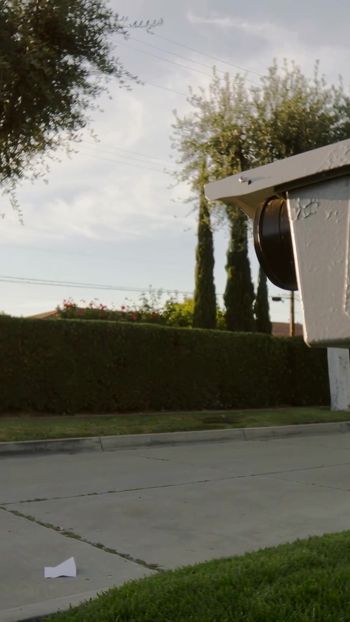 Video verticale: Telecamera che panoramica a destra, rivelando una cassetta della posta su un marciapiede suburbano con della carta, spazio per il testo