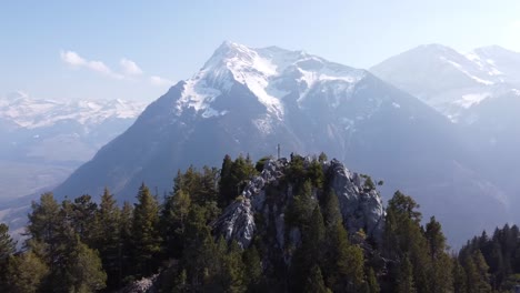 drone-flies-circle-around-a-mountain-peak-with-beautiful-lake-thun-and-swiss-alps-in-the-background,-sunny