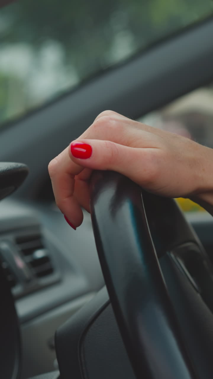Hands of woman with red nails turning steering wheel on blurred background. Female driver controls automobile driving on busy street closeup slow motion