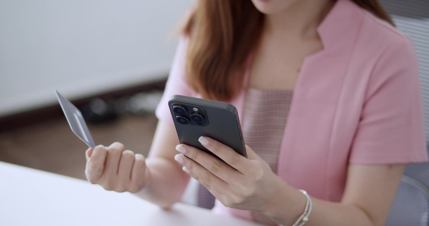 Primo piano delle mani di una donna che inserisce il numero della sua carta di credito su uno smartphone, completando una transazione di acquisto online durante una promozione speciale.