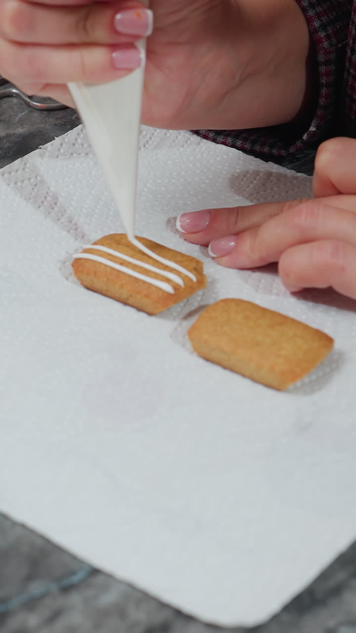 Close-up of baker decorating cookie with white icing on tissue paper, hand adorned with beaded bracelet, toothpick nearby for precise detailing