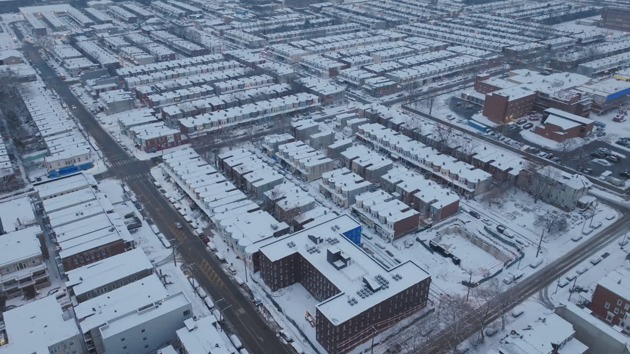Aerial drone footage panning across historic row homes in snow covered neighborhoods in West Philadelphia, Pennsylvania as cars drive down deserted streets.