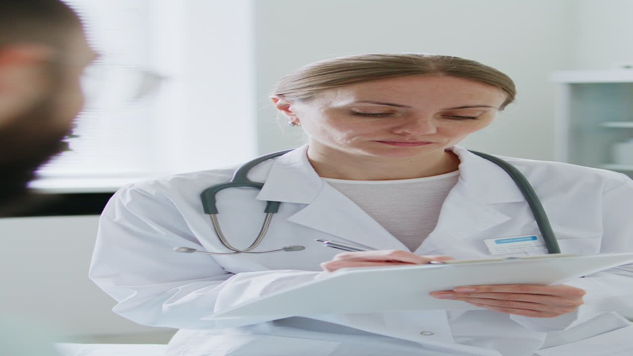 Female Doctor Talking with Patient and Writing Notes during Consultation