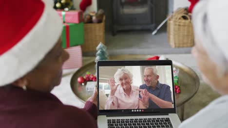 Diverse-senior-female-friends-using-laptop-for-christmas-video-call-with-happy-couple-on-screen