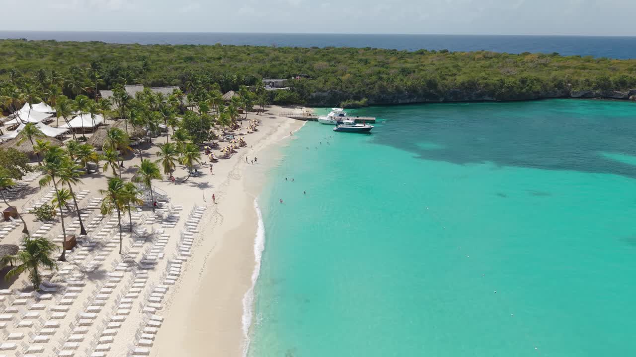Vista aérea de la playa de la Isla Catalina cerca de La Romana en la República Dominicana. Agua turquesa del Caribe, costa de arena blanca, palmeras y tumbonas de playa en un destino turístico tropical. Plano amplio.