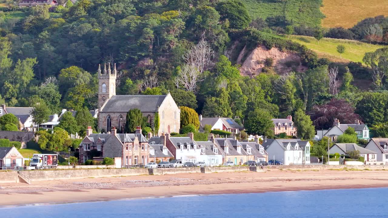 Daylight pan reveals stone church, graveyard, village homes, lush greenery, and sandy shoreline