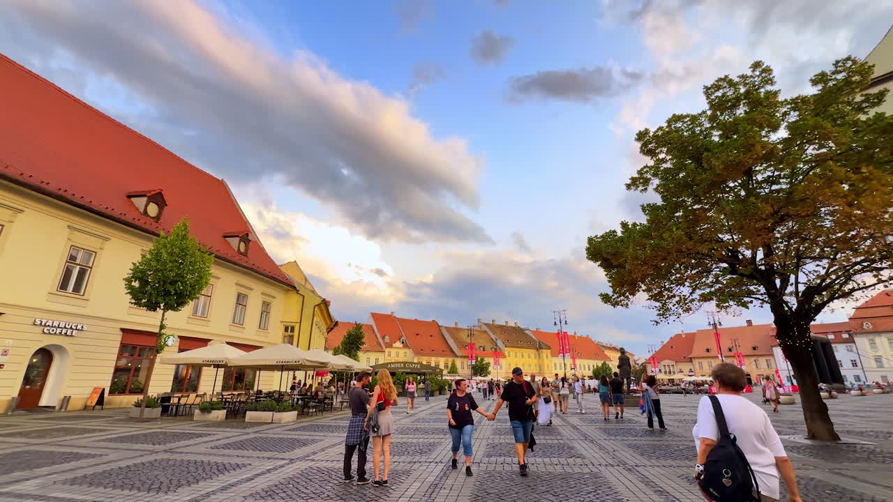 Sibiu, Romania, 17 July 2025: Crowded square in Sibiu at sunset. People stroll through Sibiu central square at sunset, surrounded by colorful historic buildings and church towers