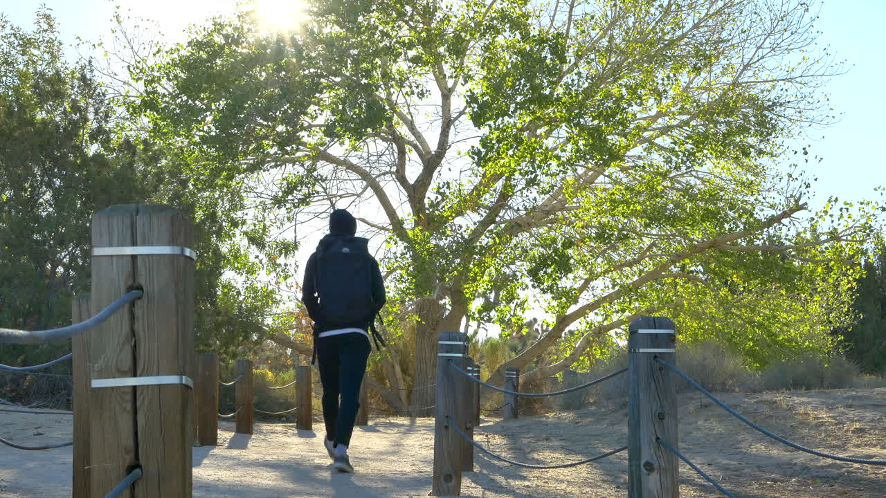 캘리포니아주 랭커스터의 일출 때 공공 사막 자연 보호 구역을 통해 혼자 하이킹하는 검은색 배낭을 메고 있는 젊은 등산객