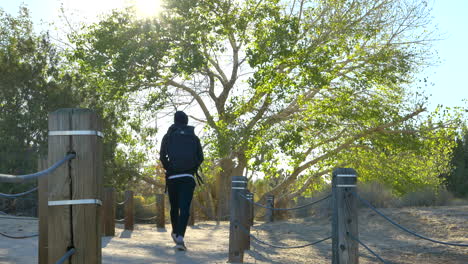 A-young-fit-hiker-with-a-black-backpack-hiking-alone-through-a-public-desert-nature-preserve-at-sunrise-in-Lancaster,-California