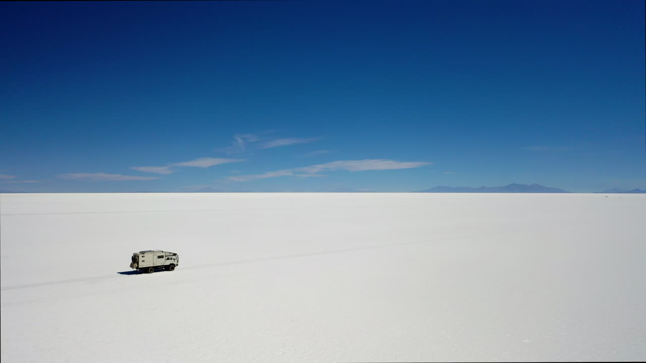 Bidikan Udara Truk Ekspedisi RV Melintasi Salar Uyuni Bolivia dengan Langit Biru dan Jalan Garam