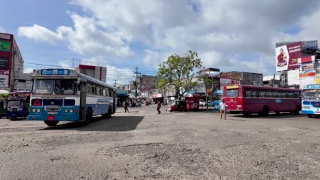 local bus stop in anuradhapura, sri lanka. the image captures buses, tuk-tuks, and people against a backdrop of urban buildings under a clear sky.