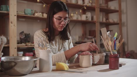 young woman potter working in art studio - finishing the final ceramic product by the table