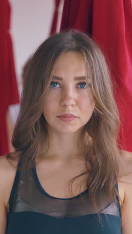 pretty young woman practices anti-gravity yoga warrior asana holding bright red hammocks and improving health close view