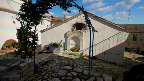 cobblestone courtyard in lefkara with a traditional archway, stone buildings, hanging plants, and a clear sky, capturing the essence of cypriot village architecture