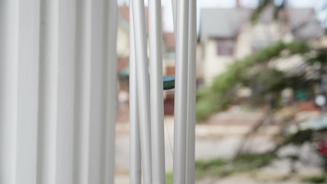Closeup of a wind chime moving in the wind with a blurred background of houses and trees on a quiet street