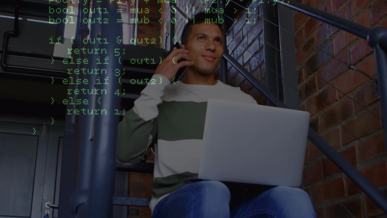 Young Man Working on Laptop and Talking on Phone with Programming Code Overlay