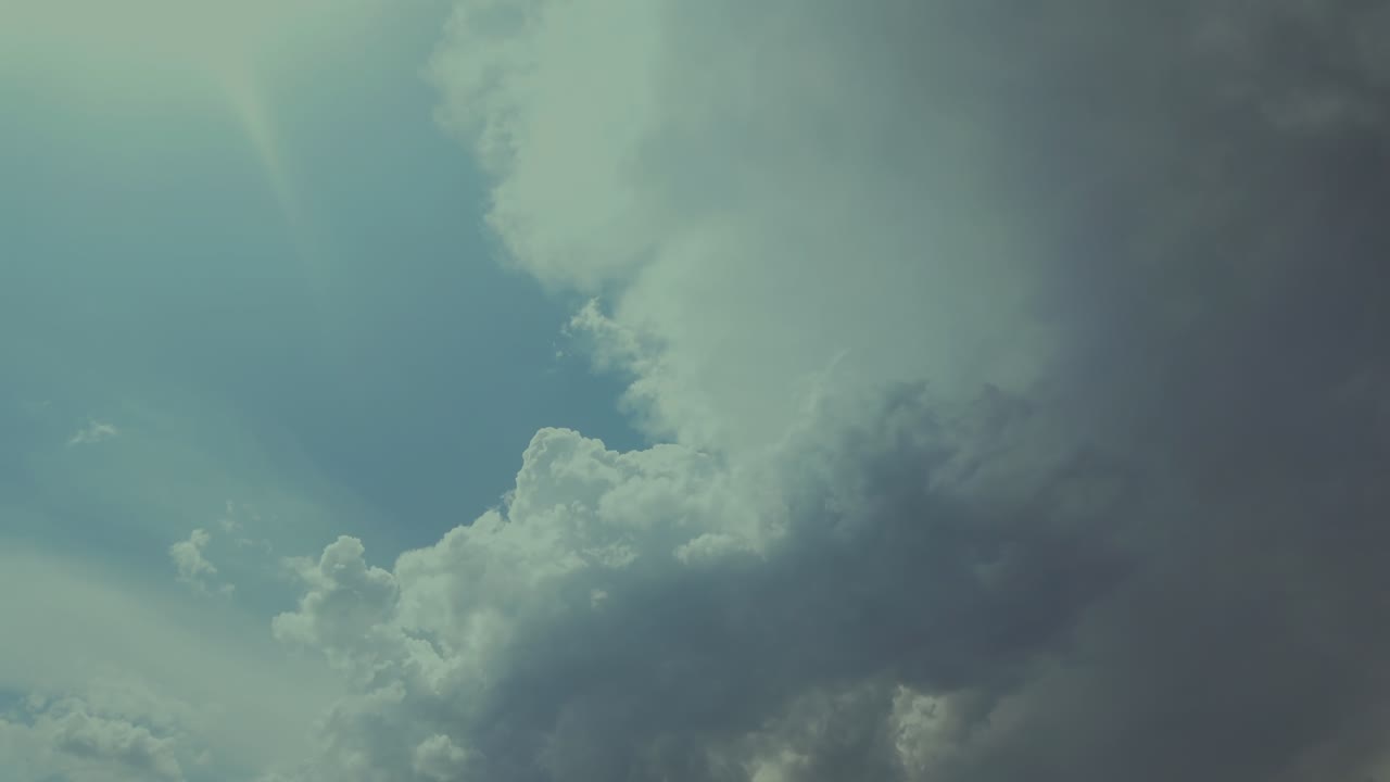 Time lapse a developing threatening storm cloud in a blue sky, with the sun rays on the left top