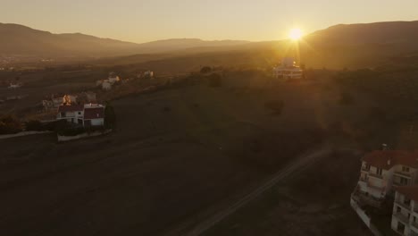 aerial view of amazing sunbeam shimmer over greek village, golden sunset tilt up