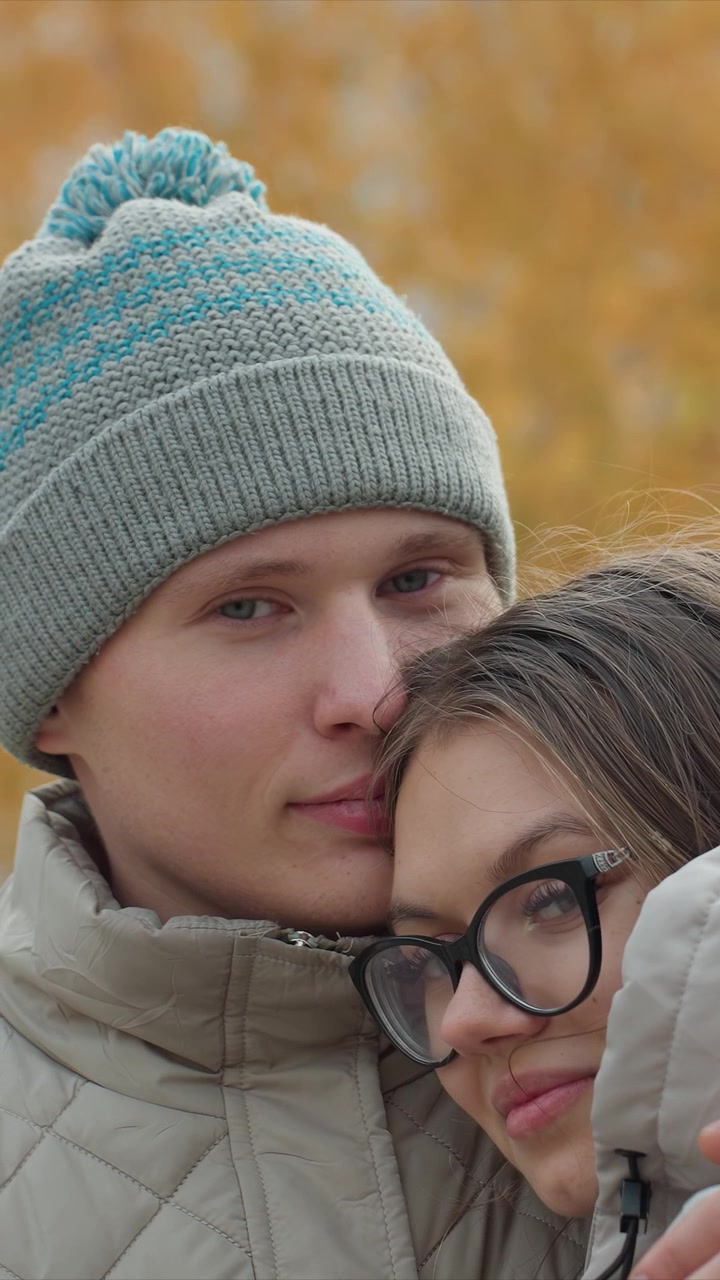 Individui con cappelli di lana rimangono fianco a fianco all'aperto. Una donna sta vicino a qualcuno che indossa un cappello blu a fantasia. Ambiente esterno con elementi autunnali stagionali presenti.