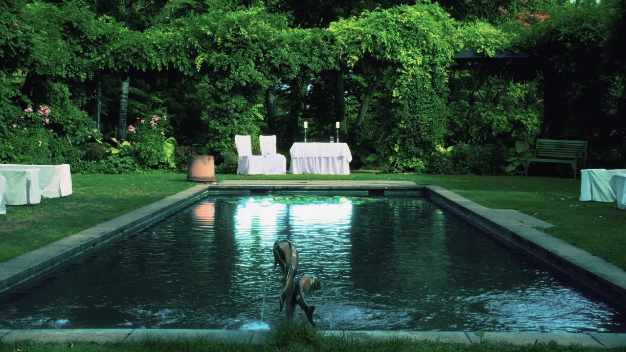 야외에 있는 외로운 아름다운 흰색 결혼 제단, 생생한 녹색 유럽 배경과 물기둥 분수가 인공 연못이나 수영장으로 졸졸 흐르는 물 표면에 아름다운 반사