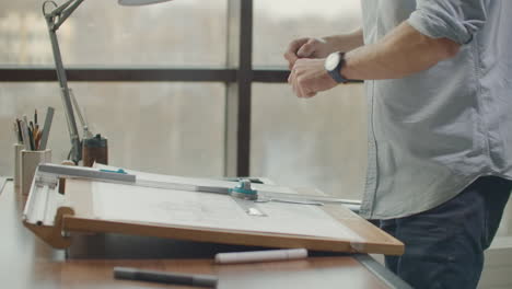 architect man standing working with blueprints sketching a construction project on wood desk at home office.construction design concept.vintage color tone. engineer works in a bright office with a large window concentrates and draws blueprints. workplace of an architect or designer: loft style minim