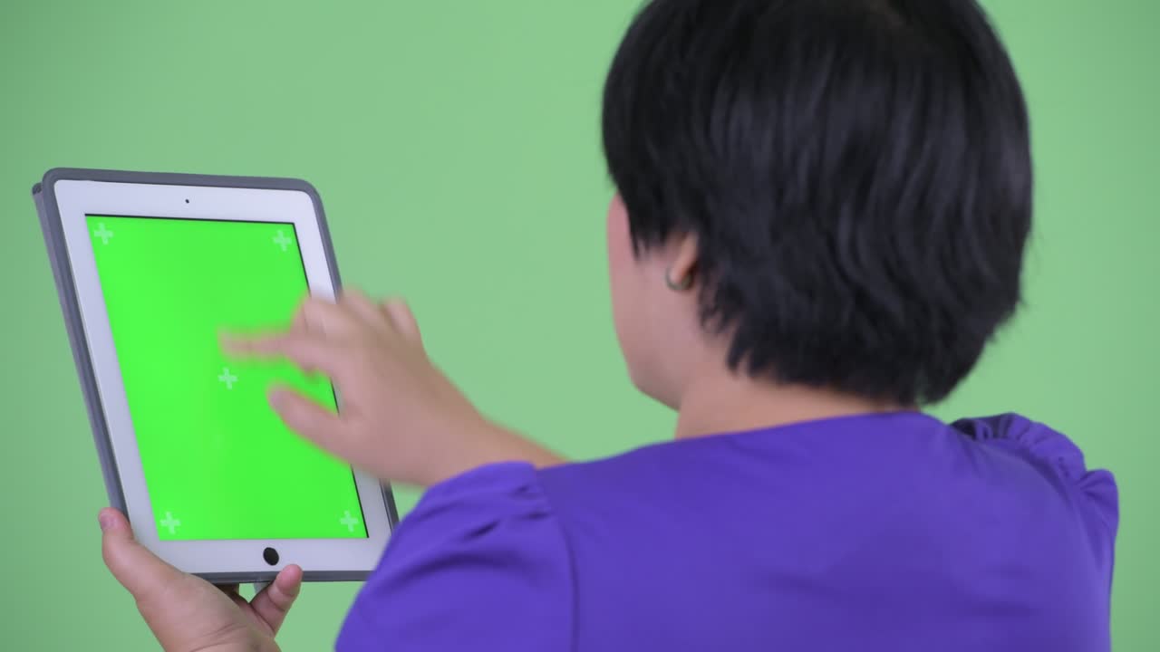 초록색 배경을 배경으로 촬영 된 크로마 키를 가진 디지털 태블릿을 사용하여 짧은 헤어 스타일을 가진 과체중 아시아 여성의 초상화