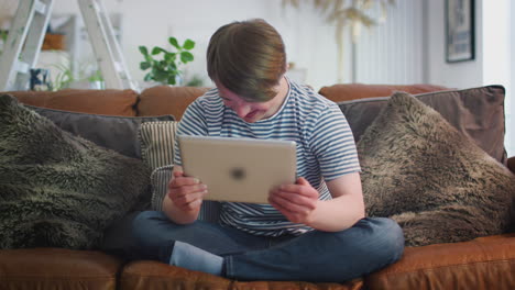 young downs syndrome man sitting on sofa watching digital tablet at home