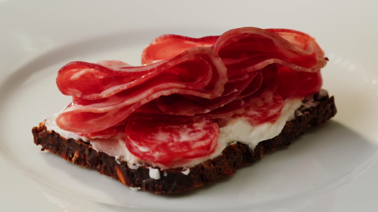 Hand placing cured meat on a sandwich