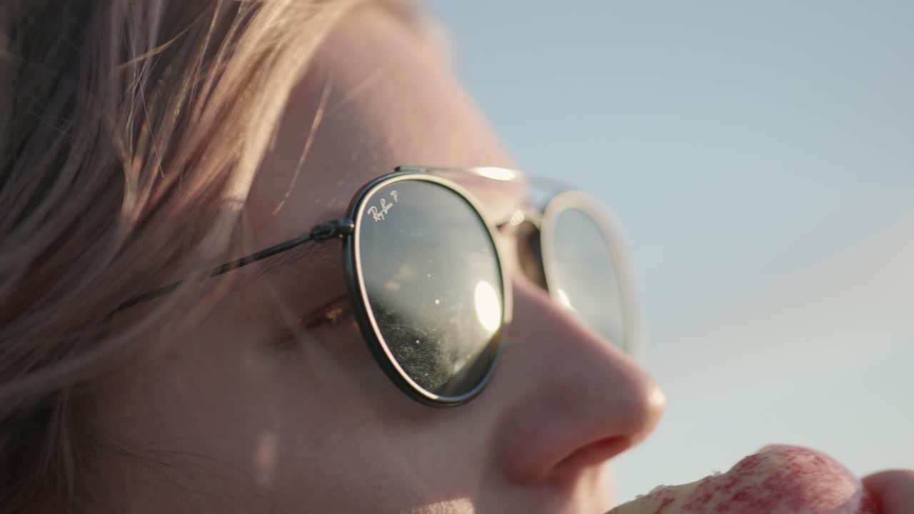 Close-up of blonde woman's face with dark sunglasses in golden hour light