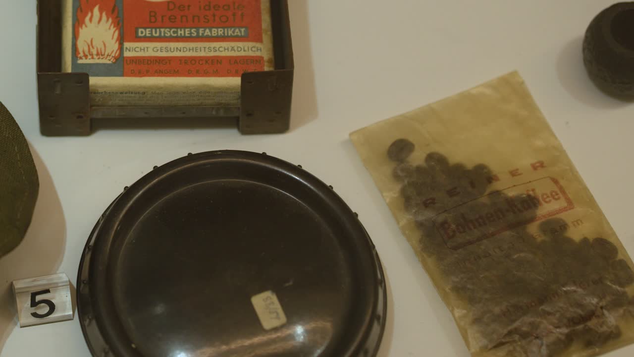 Camera slowly pans over German WWII field rations, utensils, and artifacts under museum lighting