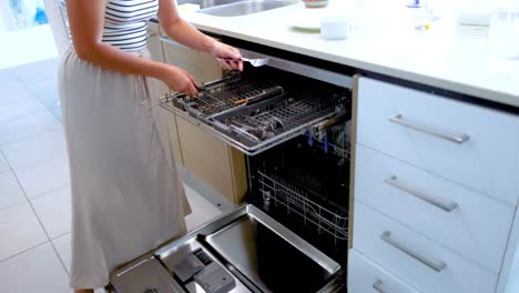 a woman loads dishes into a dishwasher in a bright, modern kitchen. the environment is clean and well-lit