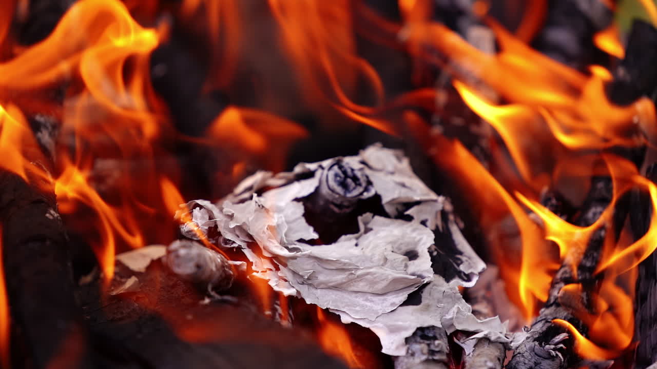 Embers of paper in fire. Bright orange flame on smoldering logs. Dancing of fire flame. Close-up. Slow motion.