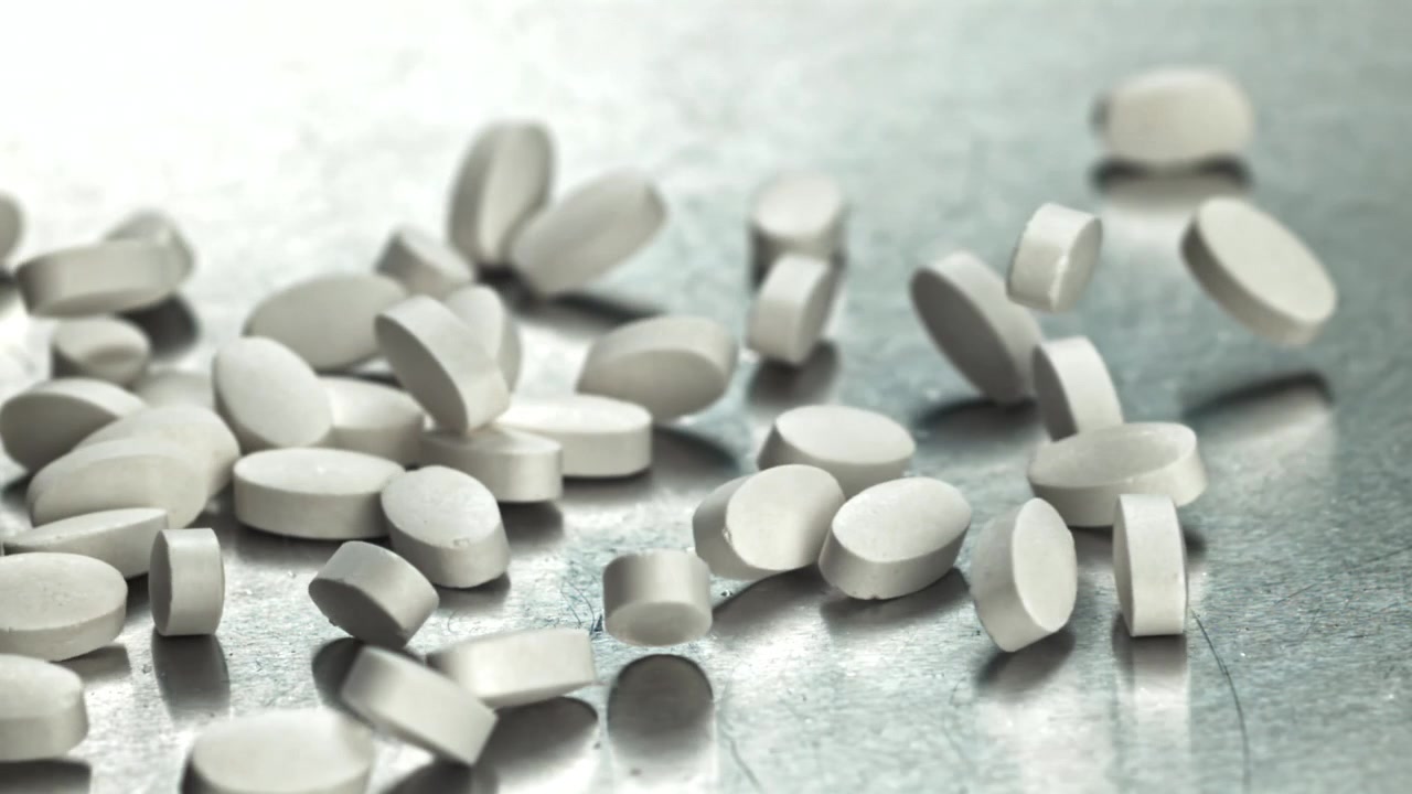White Oval Pills Falling on Metallic Surface in Slow Motion