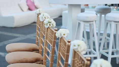 Stilvolle,-Luxuriöse-Goldene-Stühle-Mit-Weißen-Blumensträußen,-Die-Im-Wind-Schwingen,-Arrangiert-Für-Die-Hochzeitszeremonie