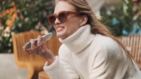 caucasian woman recording voice message on smartphone outdoors.