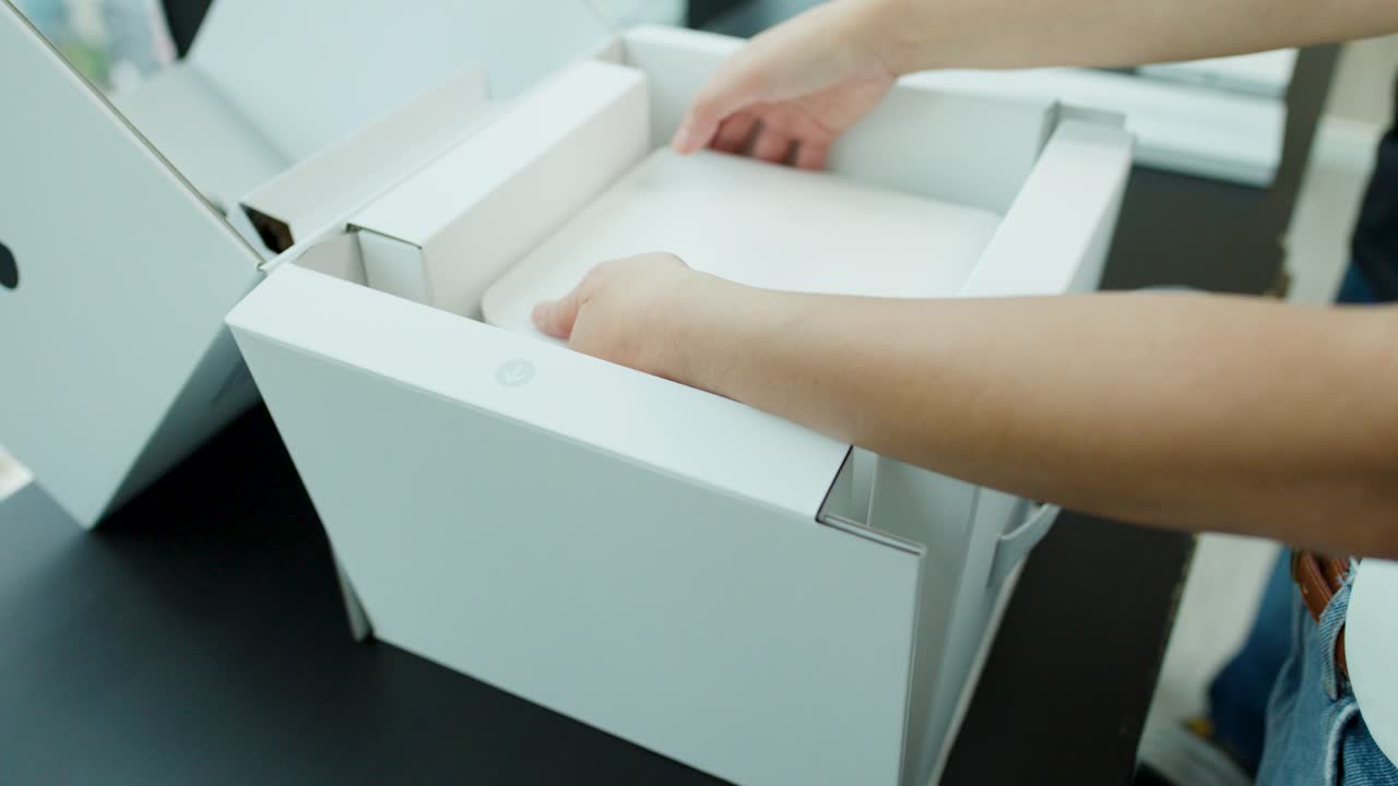 Individual removes compact desktop computer from packaging on black table in bright, natural light