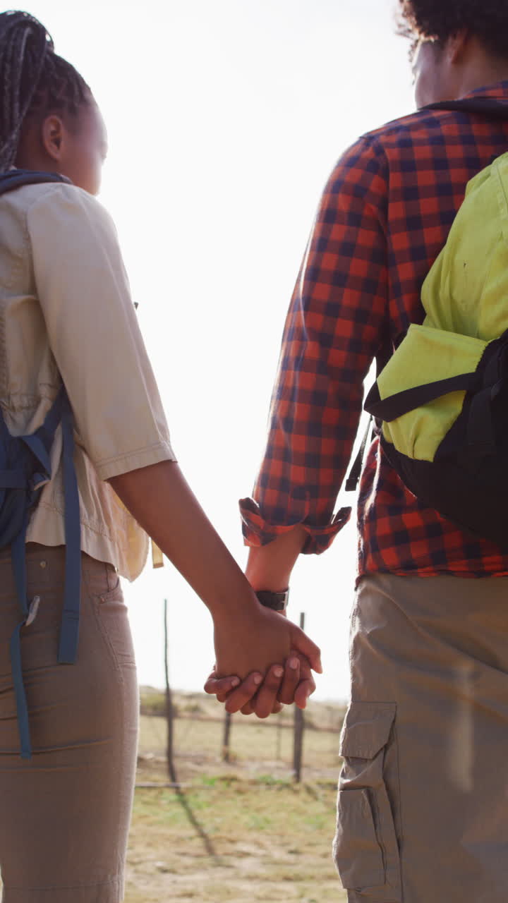 Vertical video of african american couple wearing backpack and hiking