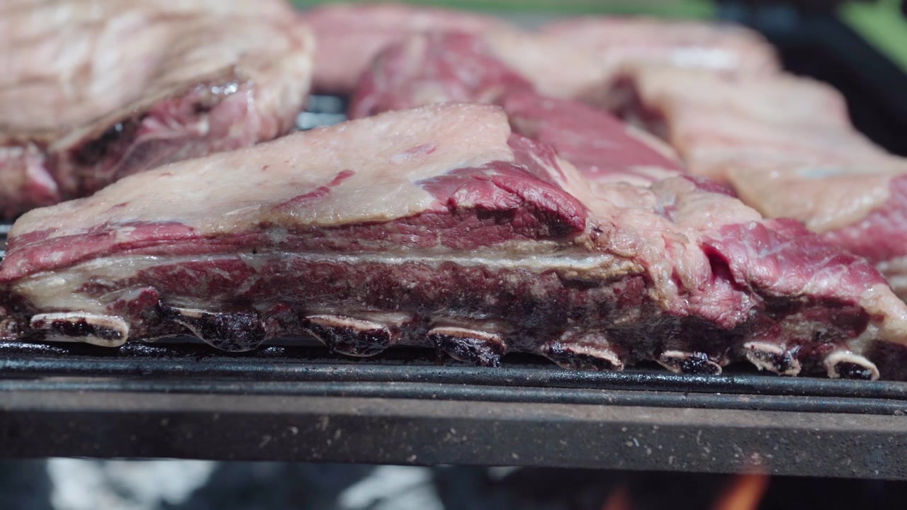 Primo piano di costine di manzo argentine che grigliano su legna da ardere durante un tradizionale barbecue asado con un'atmosfera rustica di cucina all'aperto.