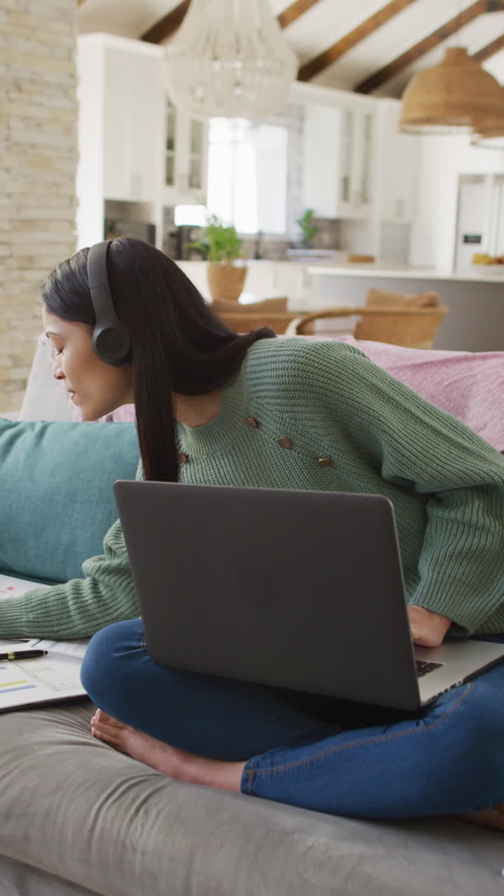 Vertical video of biracial woman using laptop and smiling
