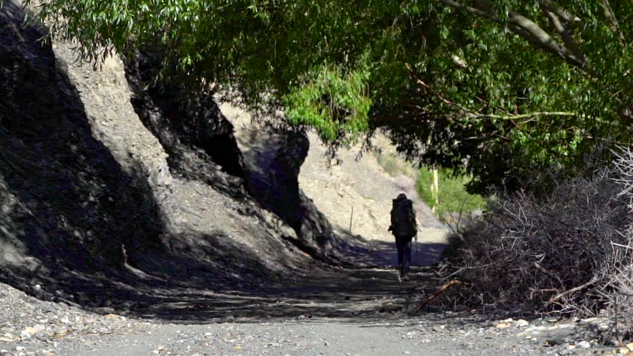화창한 날 산속의 흙길에서 배낭을 메고 그림자 속으로 걸어가는 남자