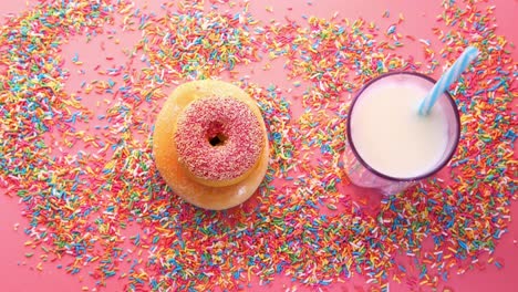 mano alcanzando una rosquilla con un vaso de leche en un fondo rosa con salpicaduras