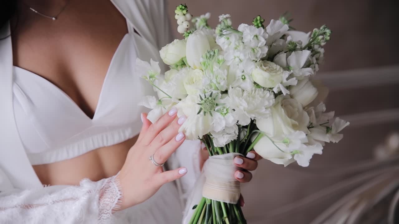 Affascinante sposa con un top bianco che tiene in mano un bouquet da sposa di rose bianche, tulipani e altri fiori.