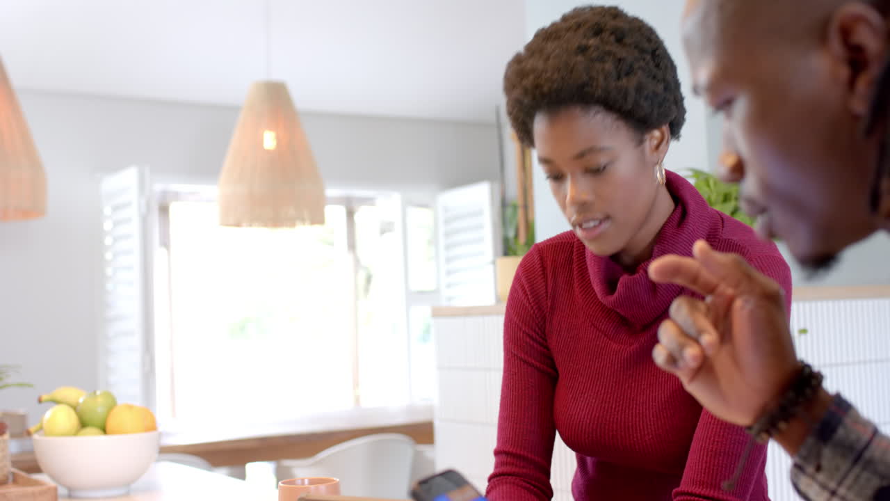 Discussing smartphone screen, African american couple working together in modern home kitchen