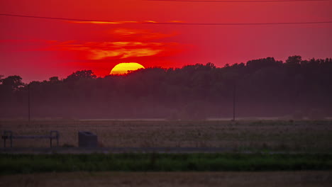 A-fiery-sunset-zoomed-in-to-show-the-glowing-sun-as-it-sets-beyond-the-golden-sky-and-forest-in-silhouette---time-lapse