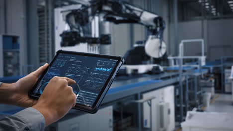 hands monitoring industrial robotics and data on a tablet in a factory setting