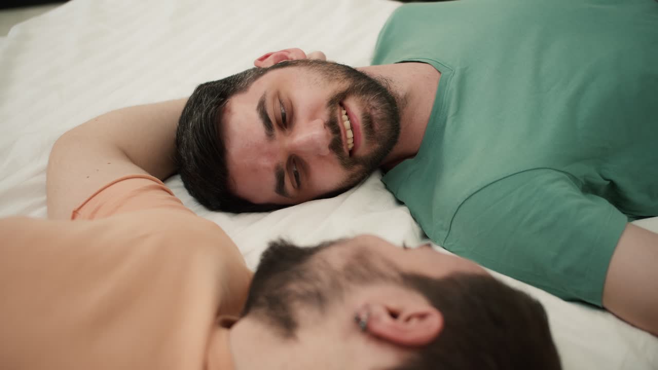 Portrait of attractive bearded gay men couples lying on bed together, touching face with romantic feeling
